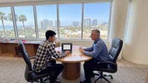 A student meets with a college counselor in San Diego to plan college applications and essays, sitting together at a desk with advising materials.